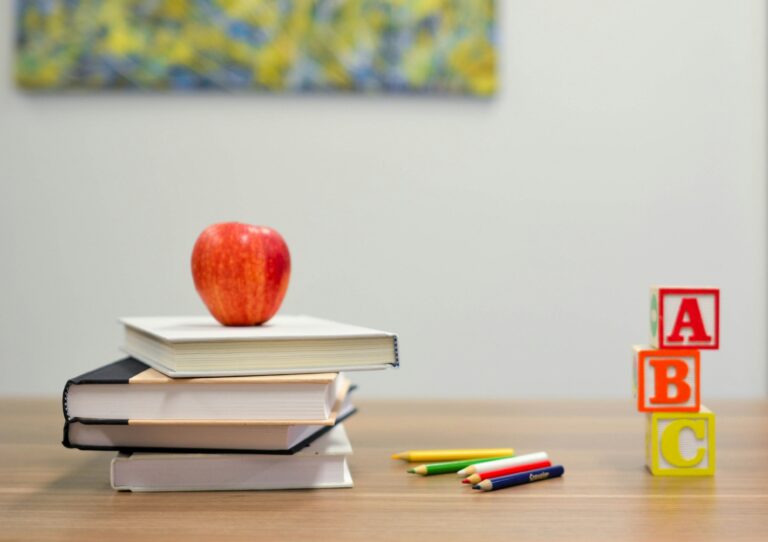 Apple on top of books next to colored pencils and three colored blocks on desk